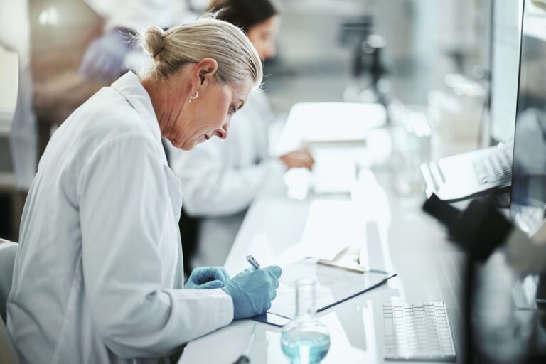 A senior female researcher, focused and diligent, writes notes while analyzing data in a modern laboratory environment. She is part of a team dedicated to developing innovative treatments aimed at improving patient outcomes worldwide. The image highlights her concentration and expertise in the field of clinical research.